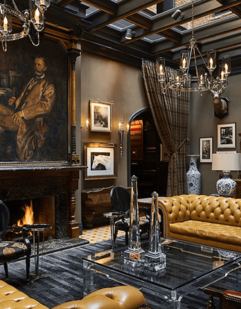 Luxurious living room with fireplace, portrait, tan leather sofas, glass table, and chandeliers.