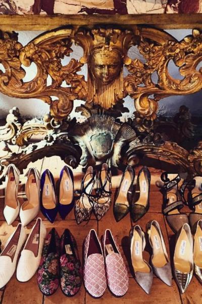 Rows of women's designer shoes on a wooden floor beneath an ornate golden sculpture.