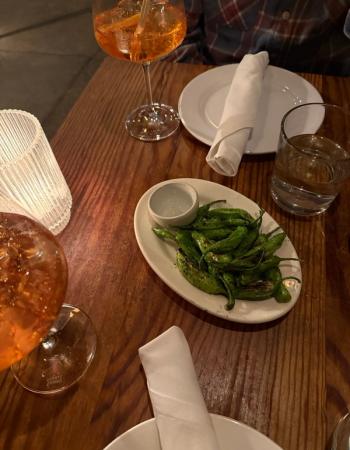 A wooden table set with two orange drinks, a plate of grilled green peppers, a glass of water, and white napkins.