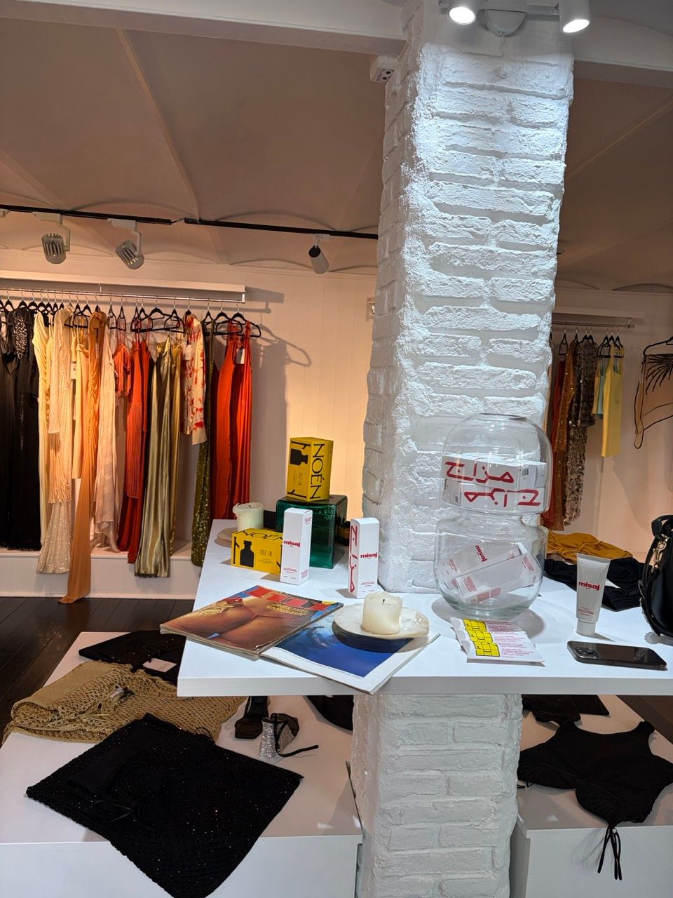 Interior of a clothing boutique with a white display table showcasing various items and racks of colorful clothing.