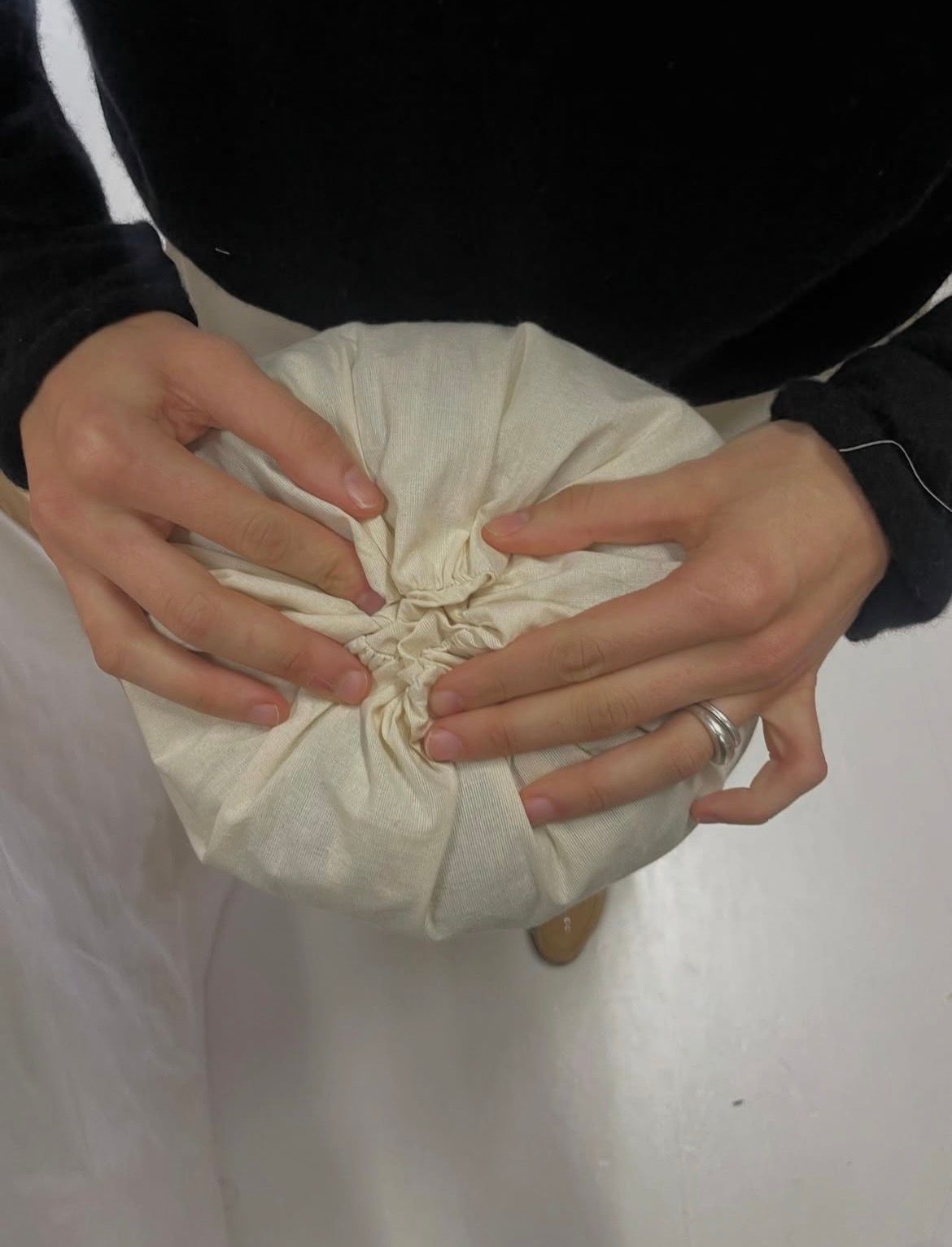 Hands gathering a cream fabric pouch.