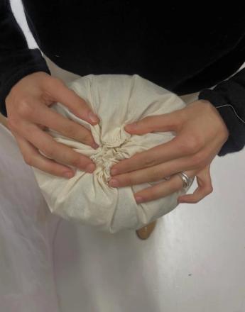 Hands gathering a cream fabric pouch.