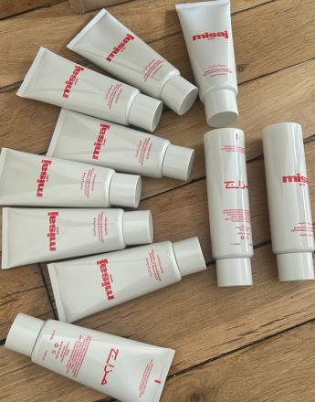 Multiple white tubes of Misaj Paris cream with red text, scattered on a wooden floor next to a cardboard box.