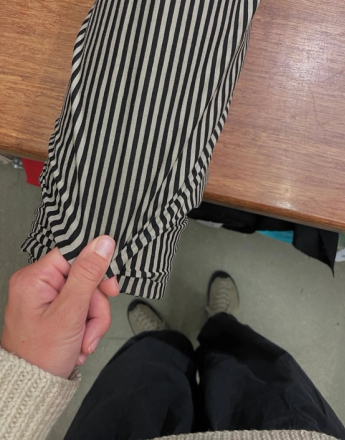 A hand holds up black and beige striped fabric, with legs in black pants and sneakers visible below.