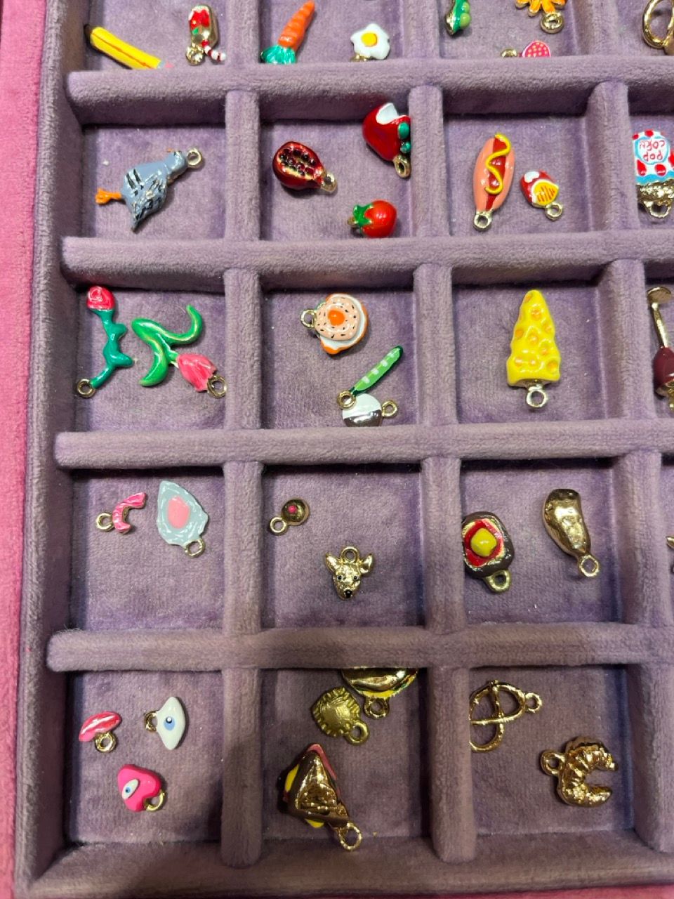 Dozens of colorful, miniature charms depicting food and objects, neatly arranged in a purple velvet tray.