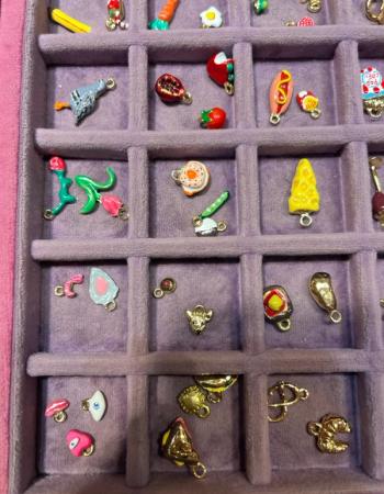 Dozens of colorful, miniature charms depicting food and objects, neatly arranged in a purple velvet tray.