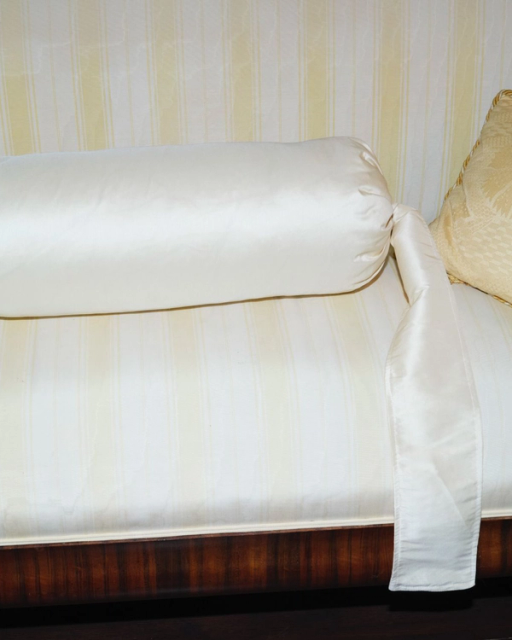 A light-striped sofa with an off-white bolster pillow with a ribbon, a cream patterned pillow, and a blue polka-dot pillow.