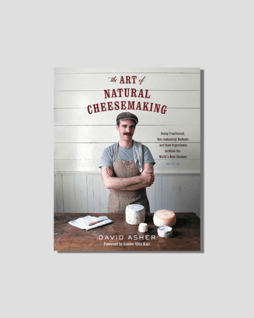Book cover for "The Art of Natural Cheesemaking" by David Asher, showing the author in an apron with various cheeses on a wooden table.