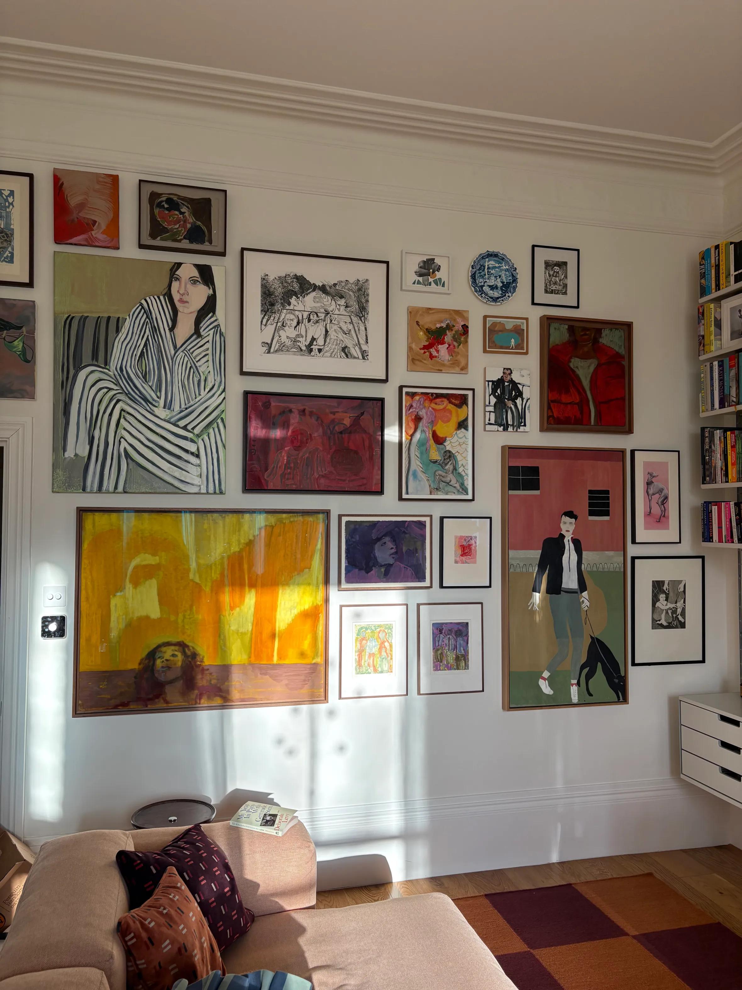 A sunny living room with a large gallery wall of diverse framed artwork and a pink L-shaped sectional sofa.