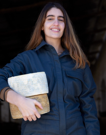A woman in a beige trench coat holds a small cleaver over her right eye.
