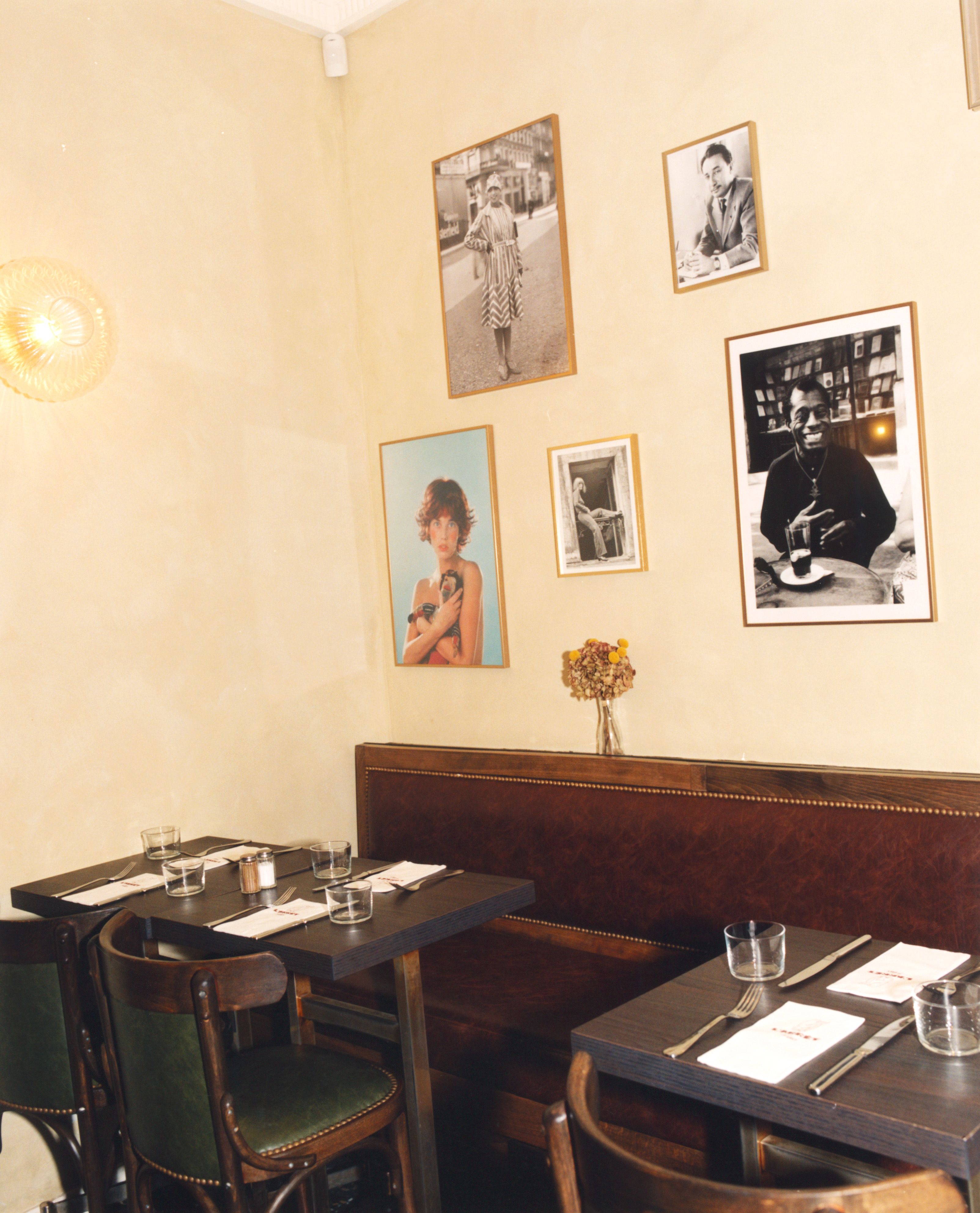 Restaurant interior with cream walls displaying framed photos, dark brown leather booth seating, and dark wooden tables set with glasses and cutlery.