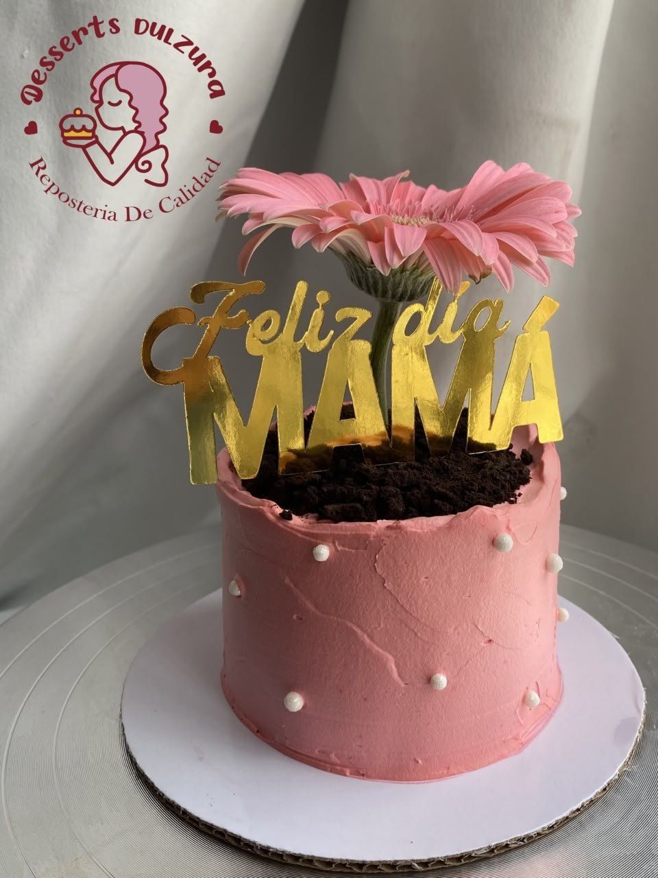 Pastel rosa con una flor natural y un letrero dorado de Feliz día mamá