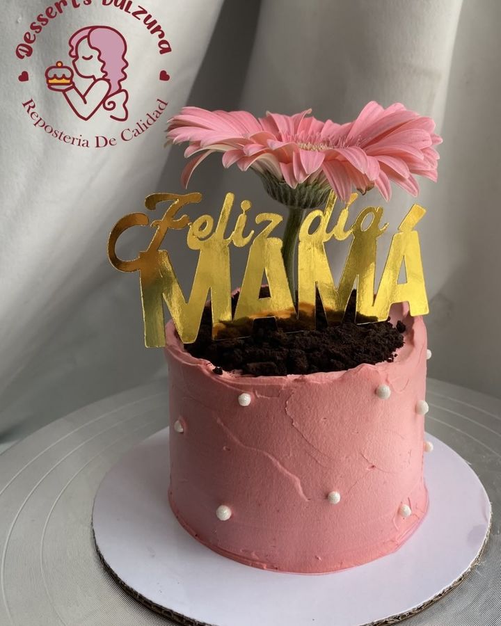 Pastel rosa con una flor natural y un letrero dorado de Feliz día mamá
