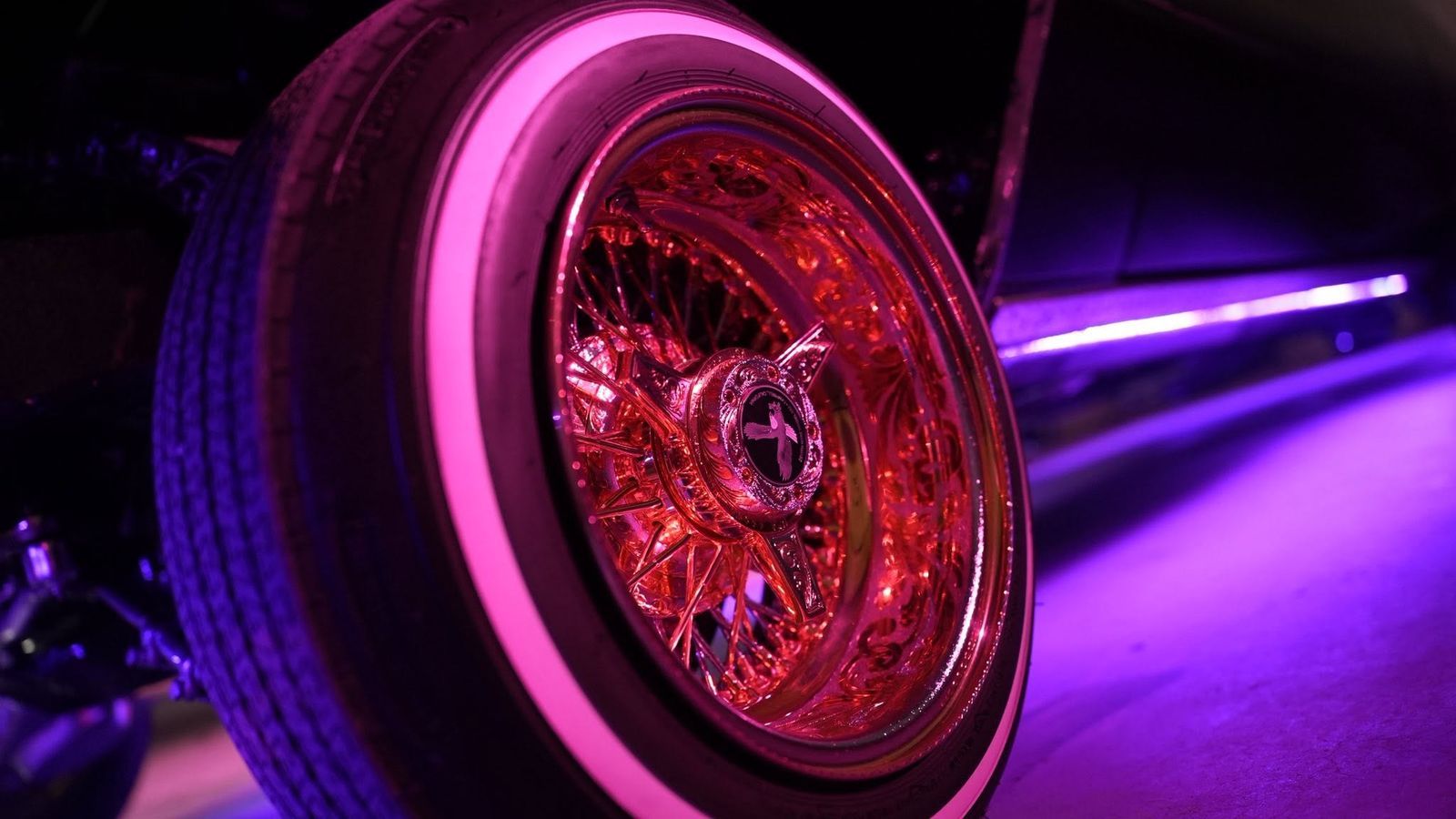 Gold wire wheel on a lowrider under neon light