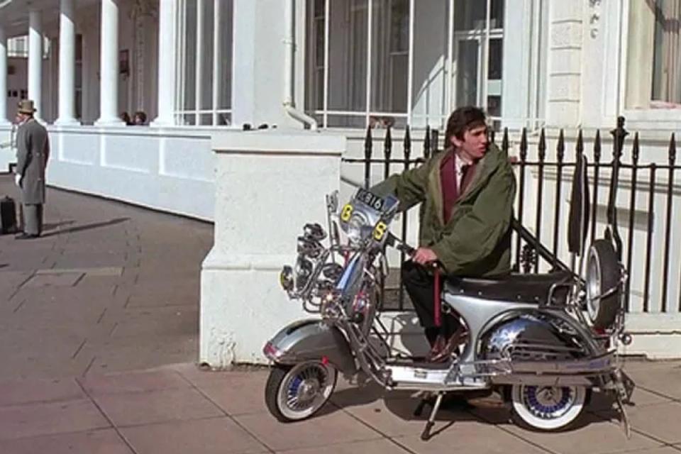 Homem usando parka por cima do terno andando de Vespa