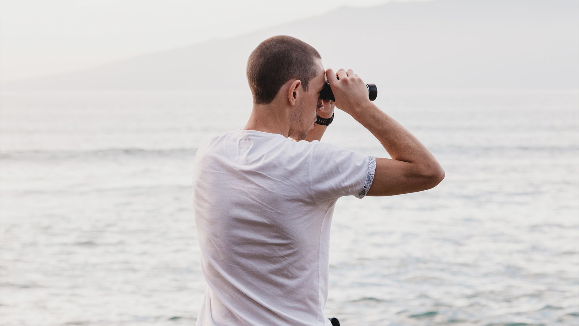 Homem olhando vista ao mar com binóculos