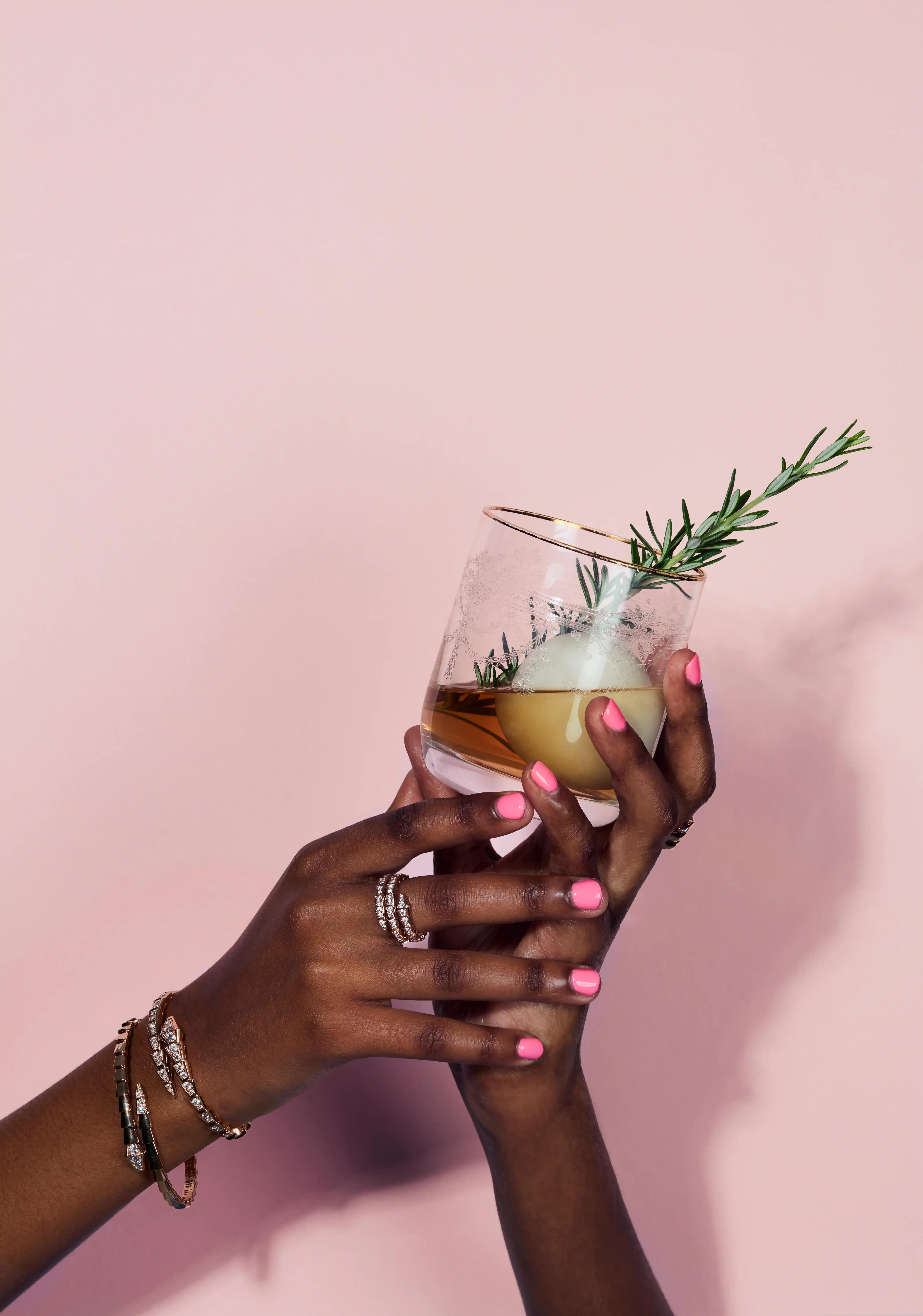 rosemary and iceball in glass with liquor in hands with jewllery