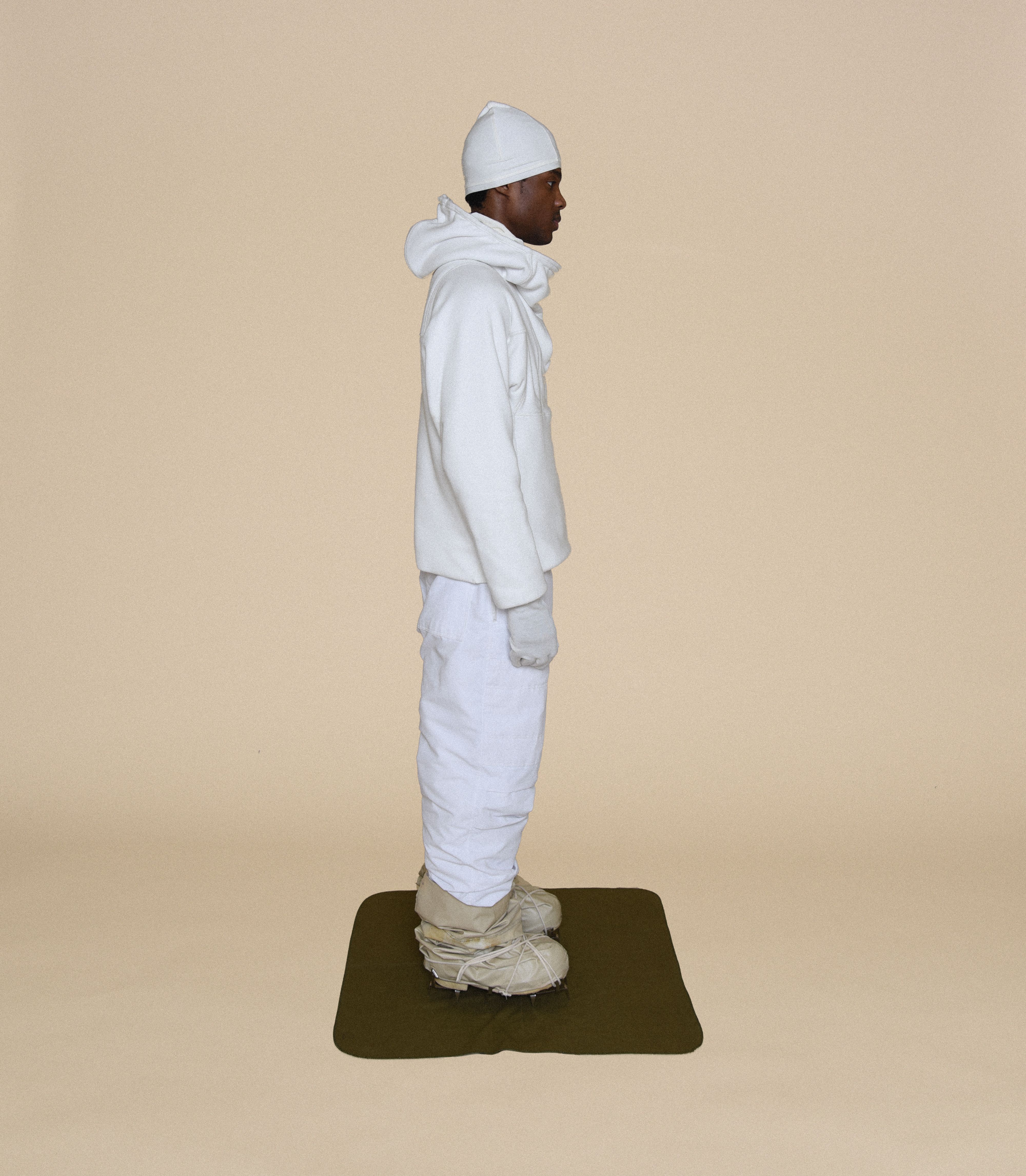 Man wearing INSULATED OVERWHITE PARKA, WIRED ARMSTRONG HOODIE, SNIPER COVER GLOVER, AIR TROUSERS and RUBBER BOOTS From Bryan Jimenez fall/winter 2023.