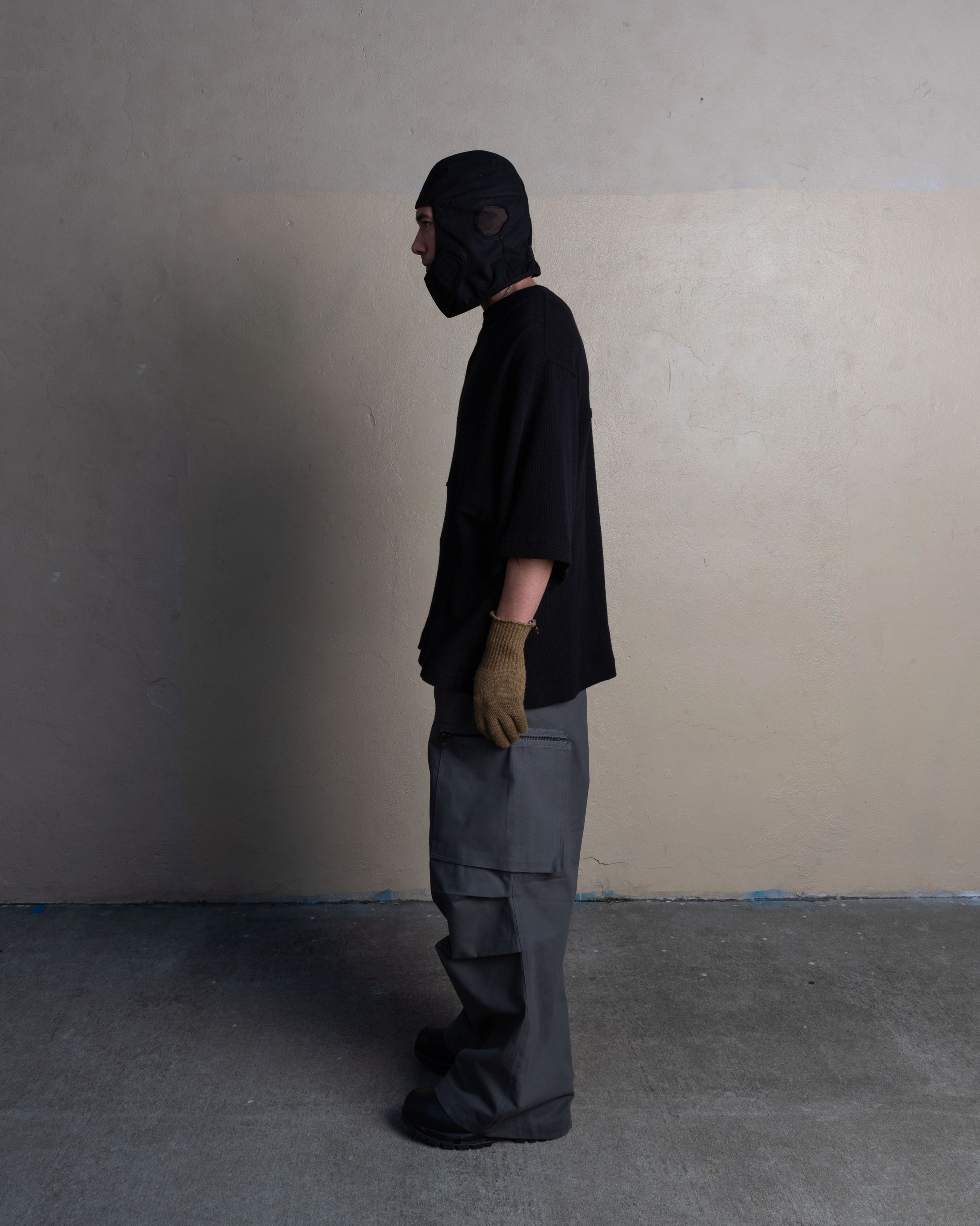 profile view of man wearing helmet liner cap, thermal tee, and cargo uniform trousers from bryan jimenez spring summer 2023