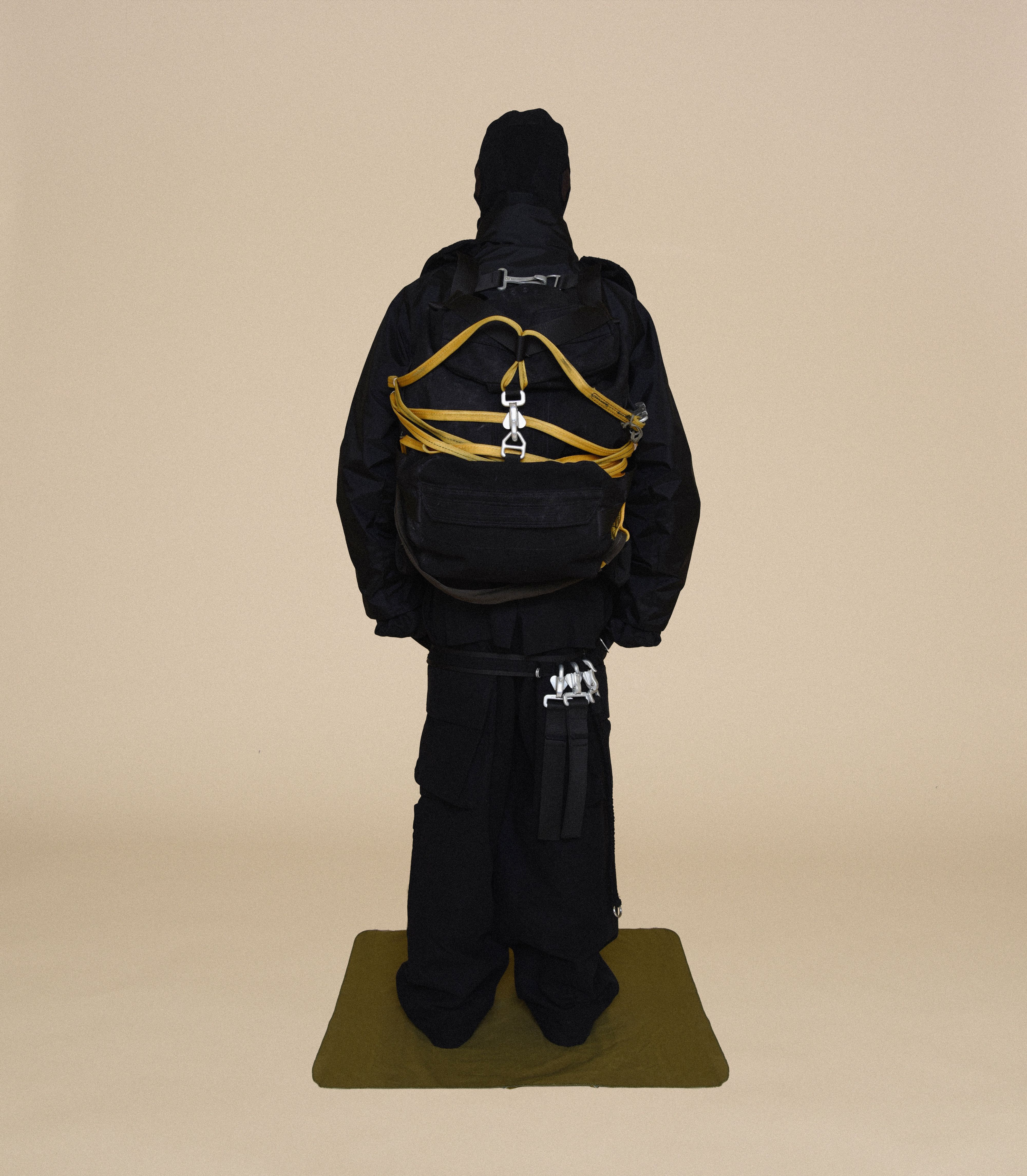 Back view of man wearing HELMET LINER CAP, COLD WEATHER PARKA, DUFFLE BAGS, BUNKER TROUSERS and COVER BOOTS From Bryan Jimenez fall/winter 2023.
