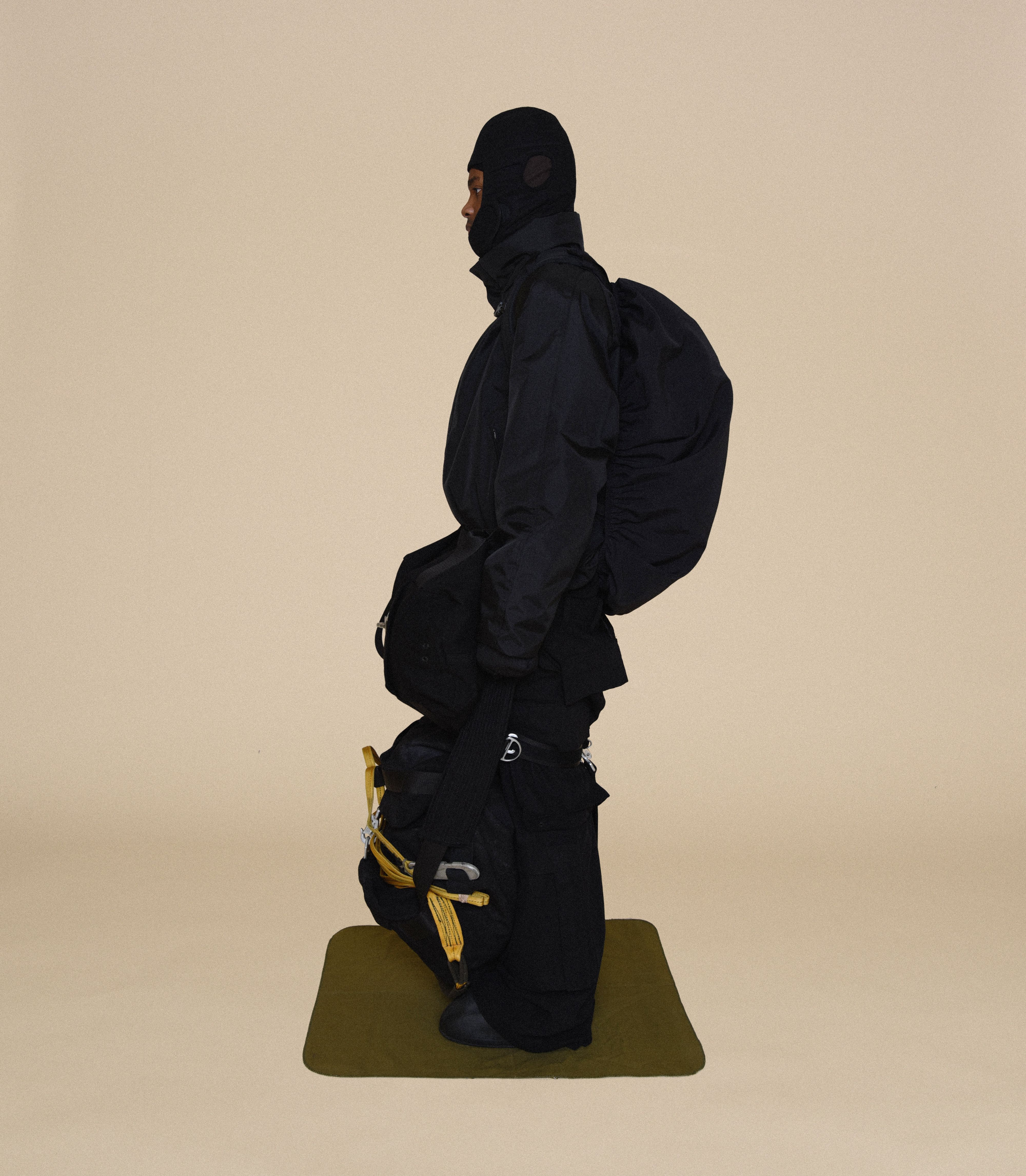Man wearing HELMET LINER CAP, COLD WEATHER PARKA, DUFFLE BAGS, BUNKER TROUSERS and COVER BOOTS From Bryan Jimenez fall/winter 2023.