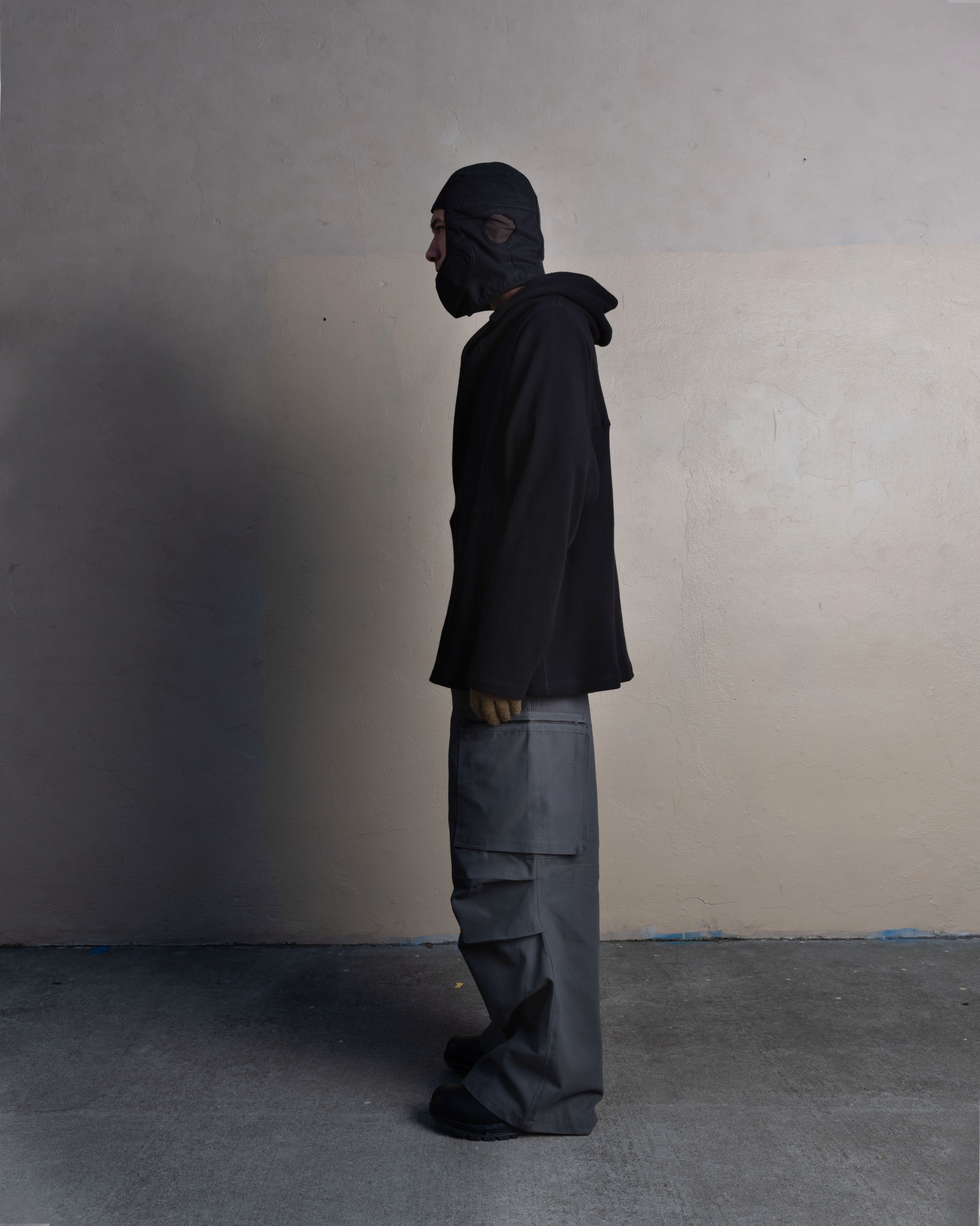 profile view of man wearing helmet liner cap, armstrong hoodie, and cargo uniform trousers from bryan jimenez spring summer 2023