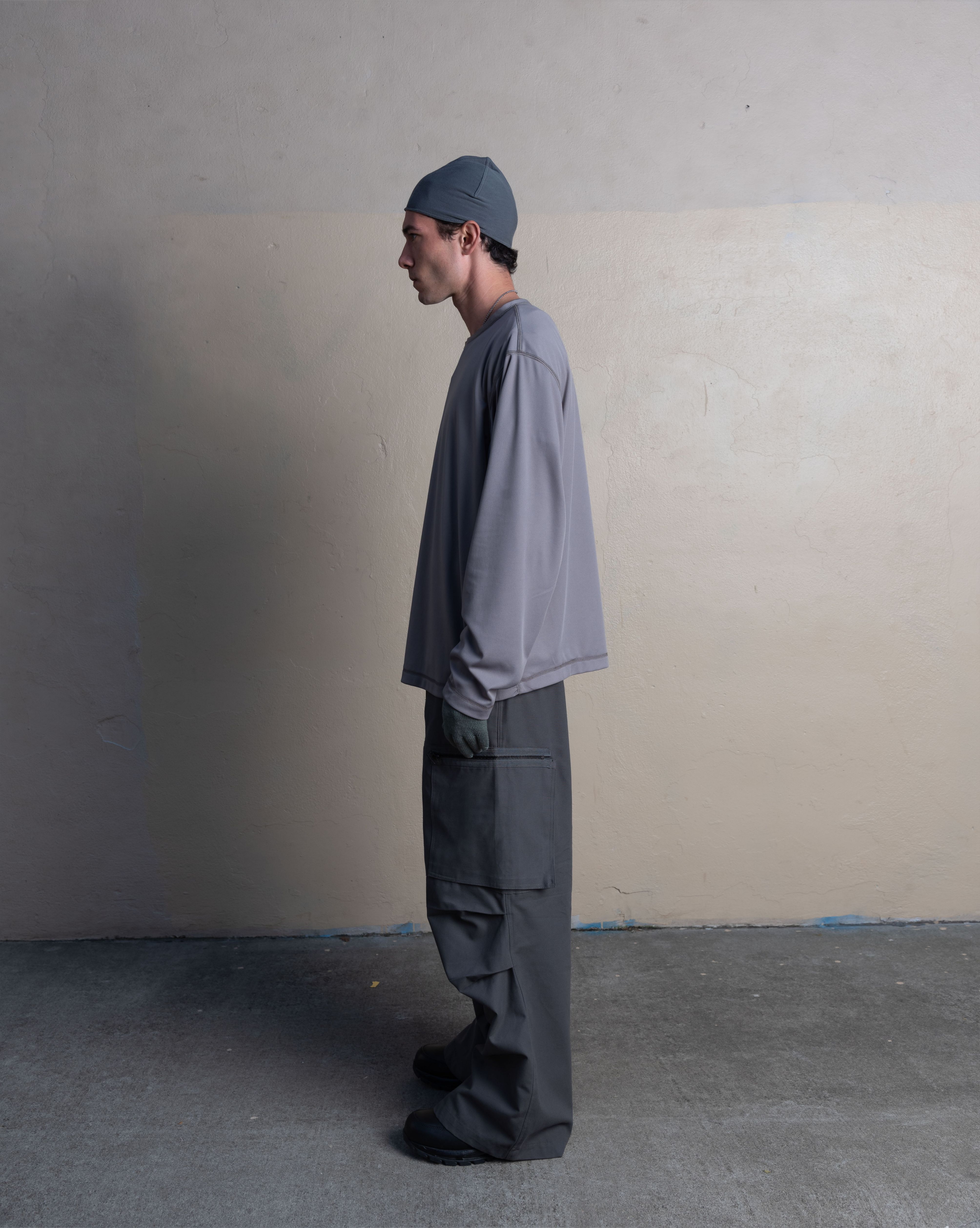 profile view of man wearing silk weight top, skull cap, and cargo uniform trousers from bryan jimenez spring summer 2023 