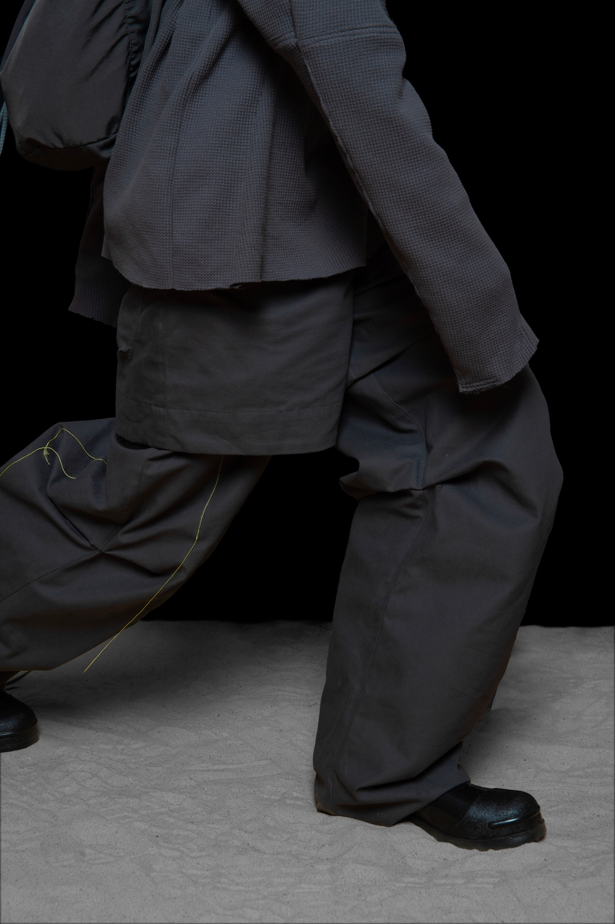 lower detail view of man wearing head liner cap, oxygen hoodied vest bag, thermal jumper, and layered trouser from bryan jimenez fall winter 2020