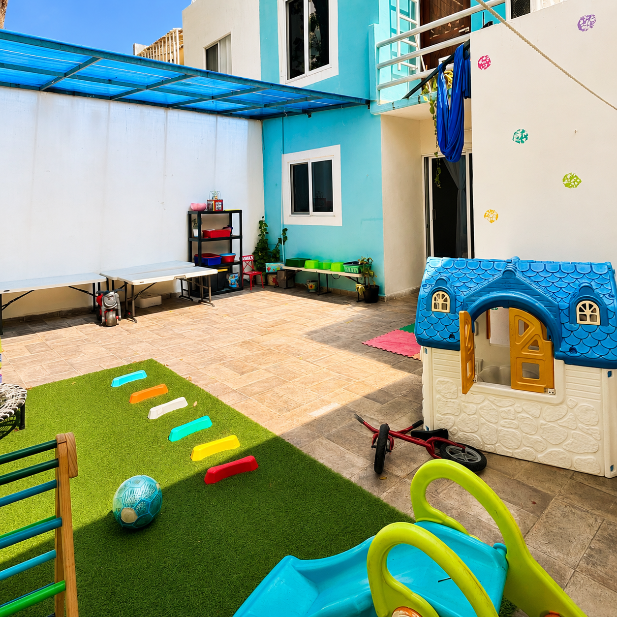 Patio al aire libre con casita de juegos, pasto y área de psicomotricidad