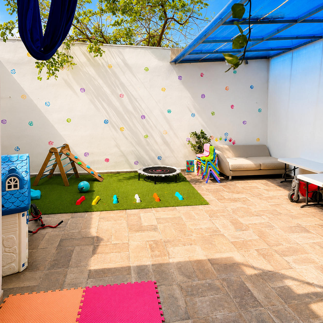 Patio con trepador de madera, tapete de pasto y muro decorado con manos pintadas por los niños