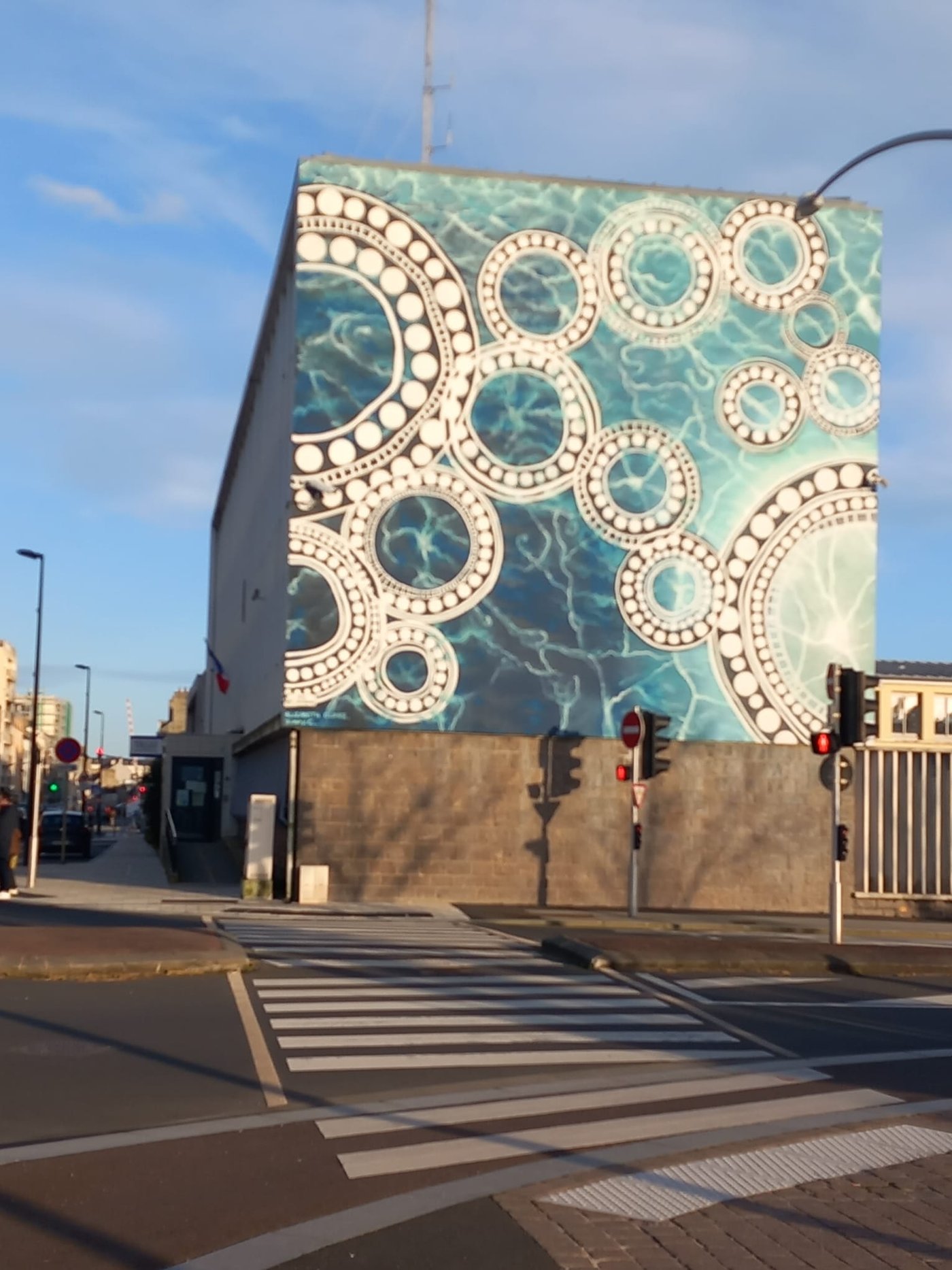 Photo : Justine Lefevre. 2026. Localisation: quai de l’entrepôt. Il s’agit d’un des murs de l’ancien commissariat. Les artistes  australiens à l’origine de cette réalisation ont voulu explorer le lien entre Port Adelaide Enfield et Cherbourg, et effectué un travail autour de l’eau et du  mouvement en 2019.