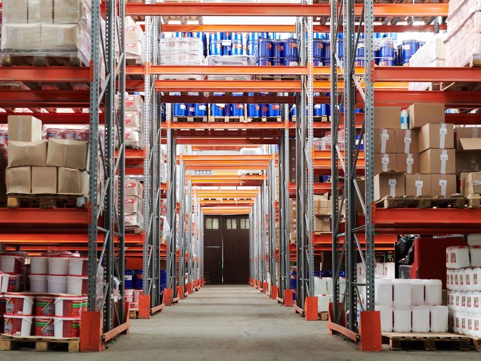 Corsia di un magazzino di distribuzione con scaffalature rosse cariche di pallet, cartoni e fusti