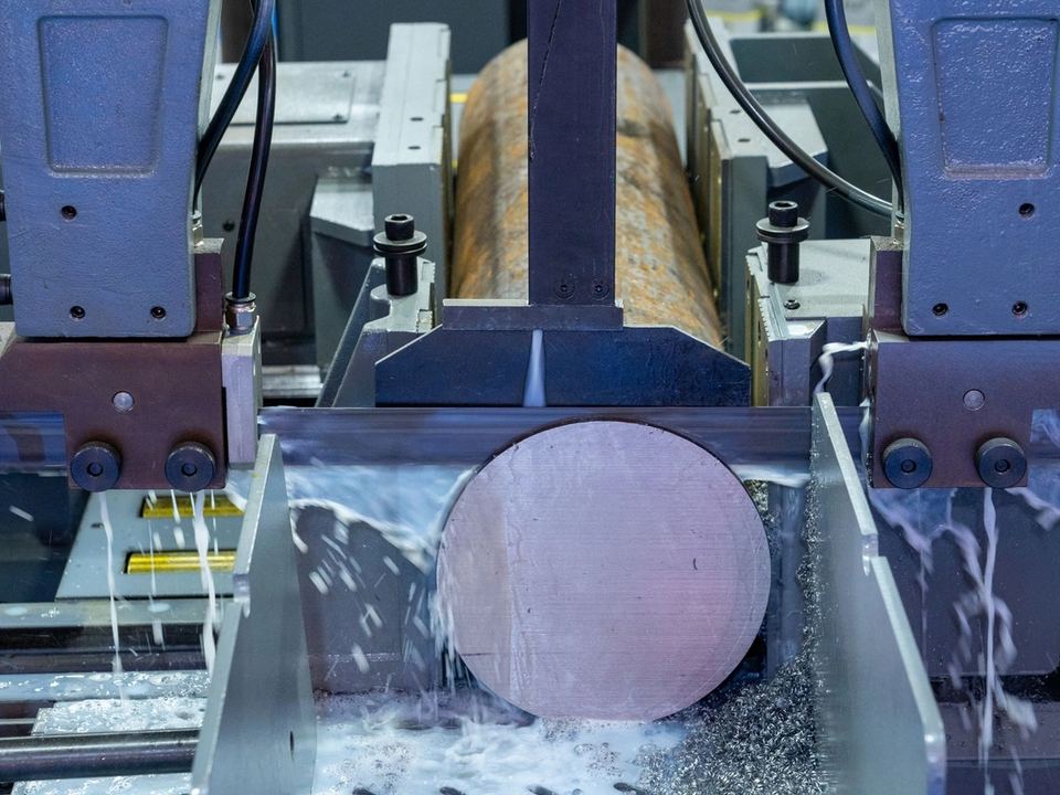 Sega a nastro industriale che taglia una barra d'acciaio, con il getto del liquido refrigerante