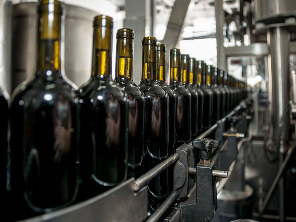 Bottiglie di vino scuro senza etichetta allineate su una linea di imbottigliamento in cantina