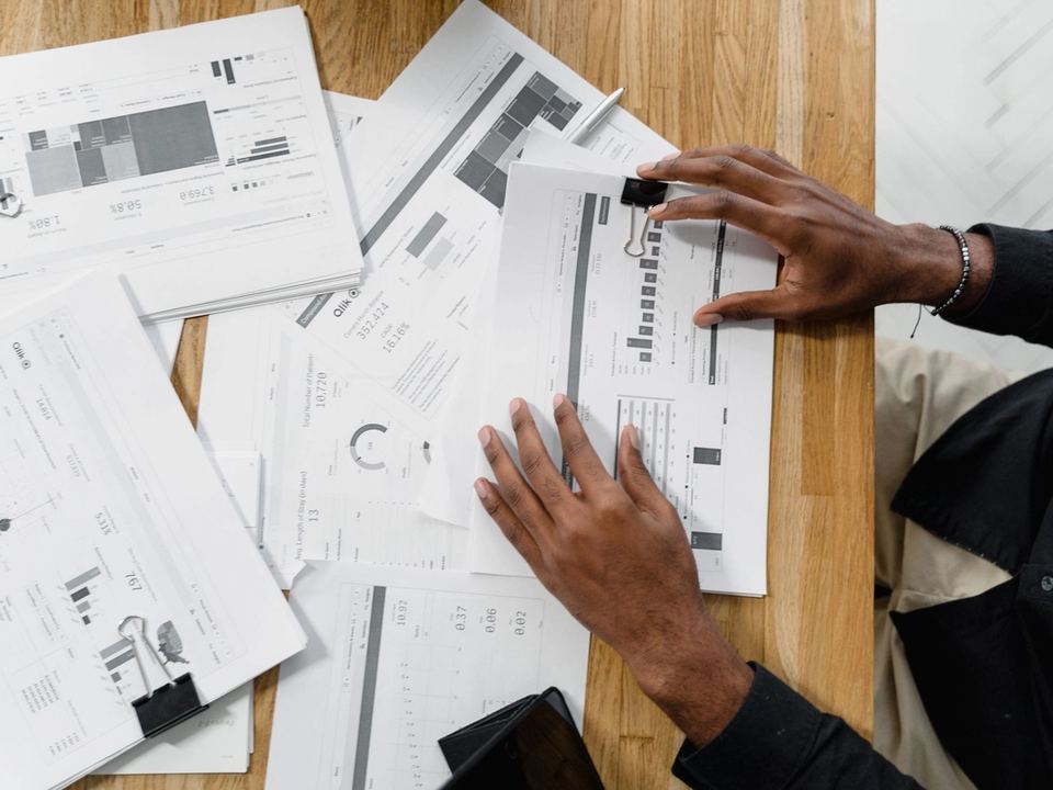 Mani che esaminano documenti finanziari con grafici e tabelle su un tavolo di legno