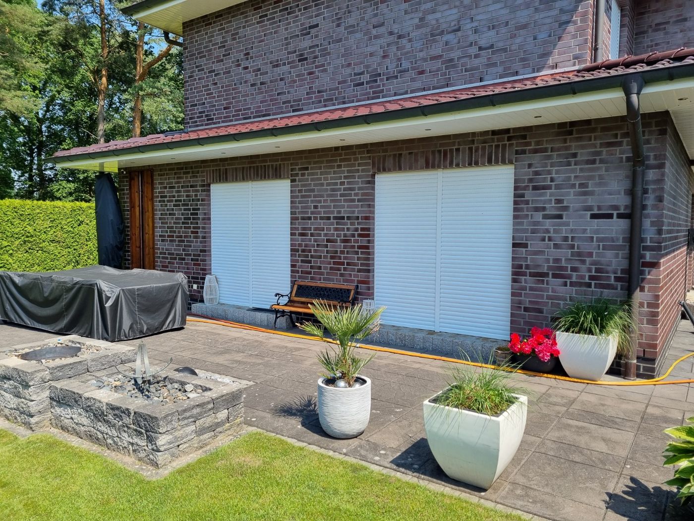 Gepflasterte Terrasse vor einem Wohnhaus mit Backsteinfassade ohne zusätzliche Terrassenüberdachung.