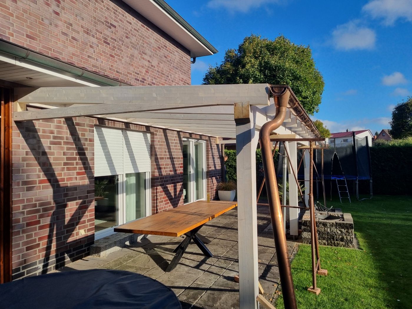 Seitliche Ansicht der hellen Terrassenüberdachung aus Holz mit Dachsparren und Dachrinne.