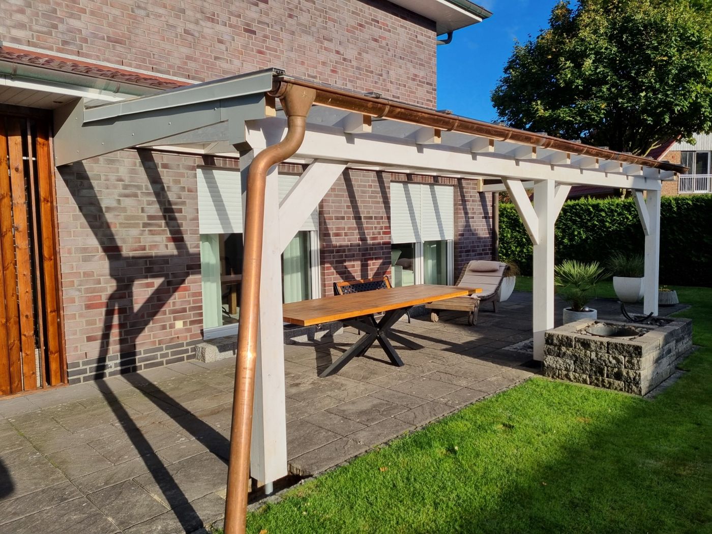 Fertiggestellte Terrassenüberdachung aus heller Holzkonstruktion an einem Wohnhaus mit Backsteinfassade.