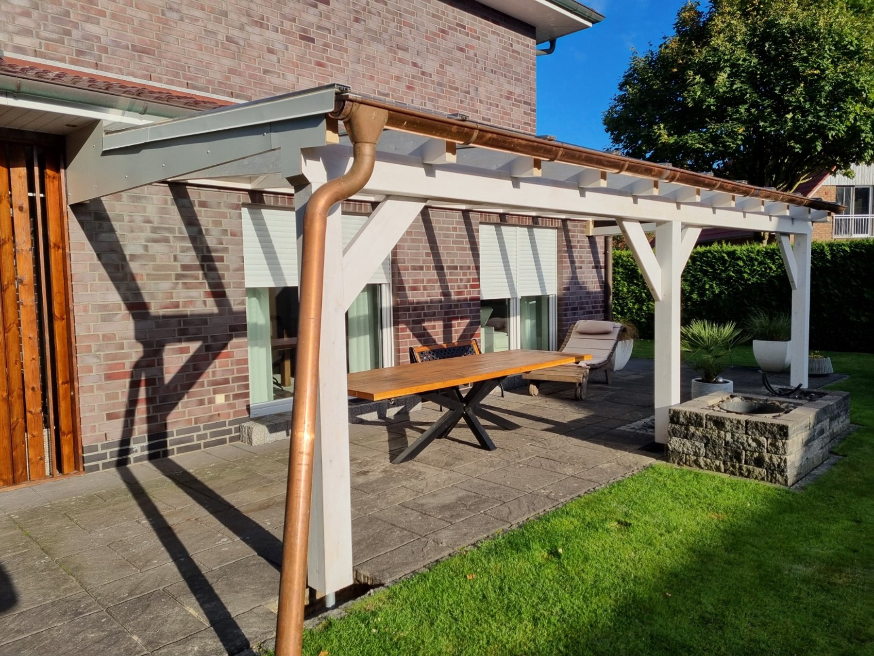 Fertiggestellte Terrassenüberdachung aus heller Holzkonstruktion an einem Wohnhaus mit Backsteinfassade.
