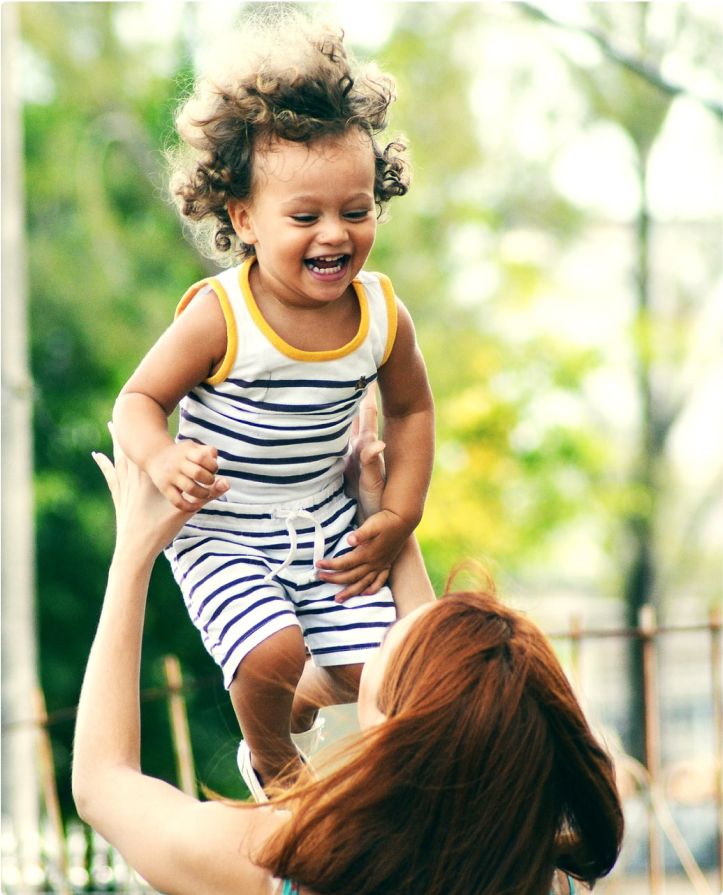A mother playfully tosses a happy child in the air above her.