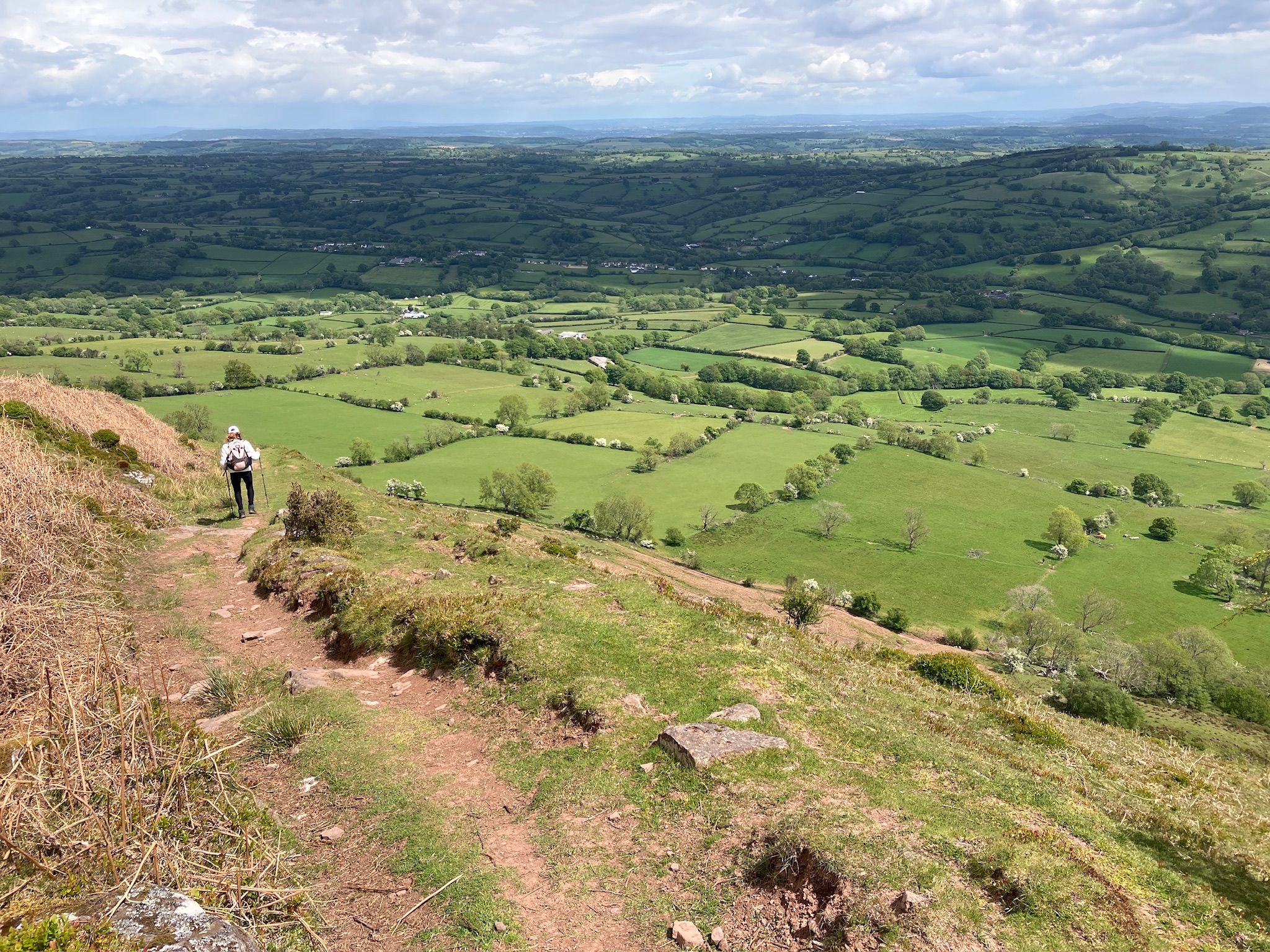 Walker descending the Offa’s Dyke Path with wide views across rolling farmland.