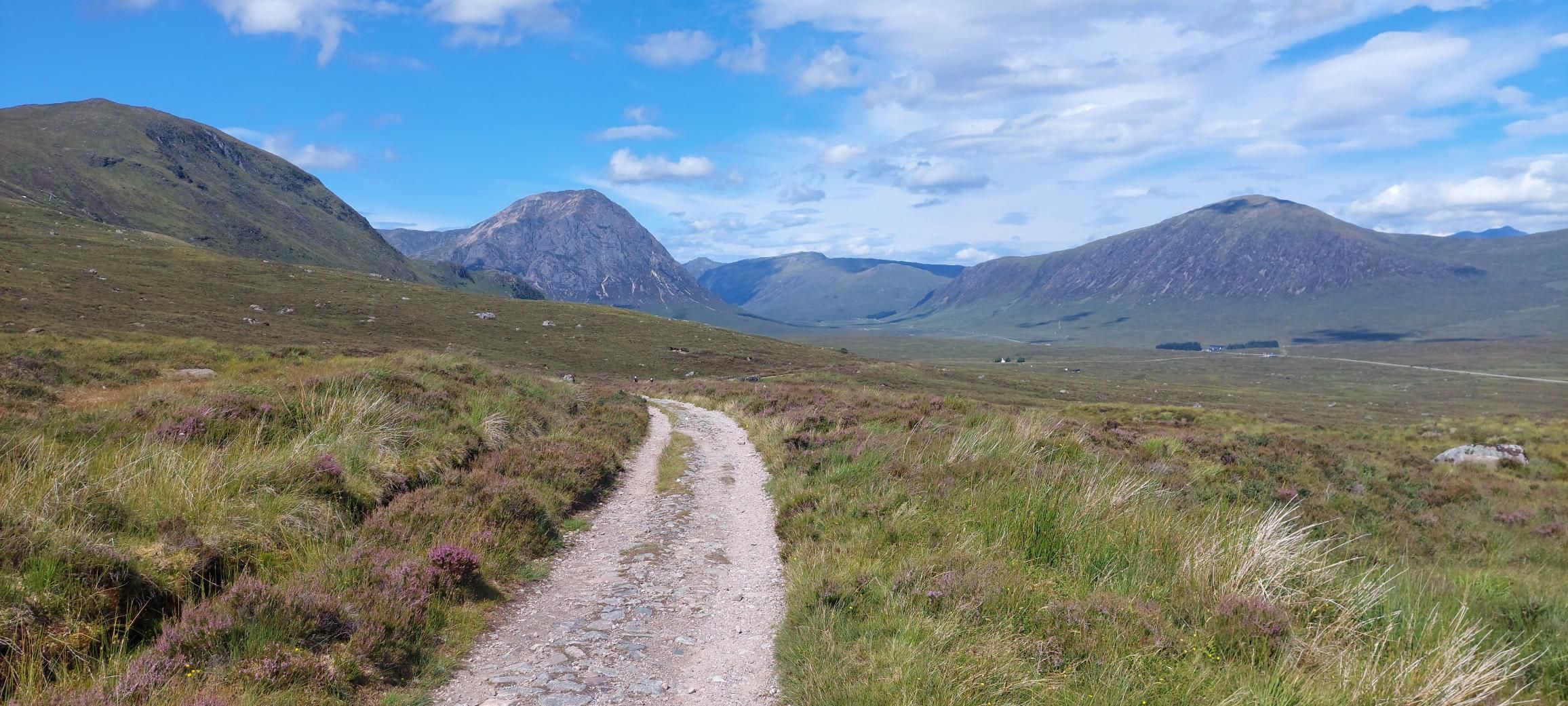 Broad stony track crossing open moorland on the West Highland Way, with Highland mountains ahead.