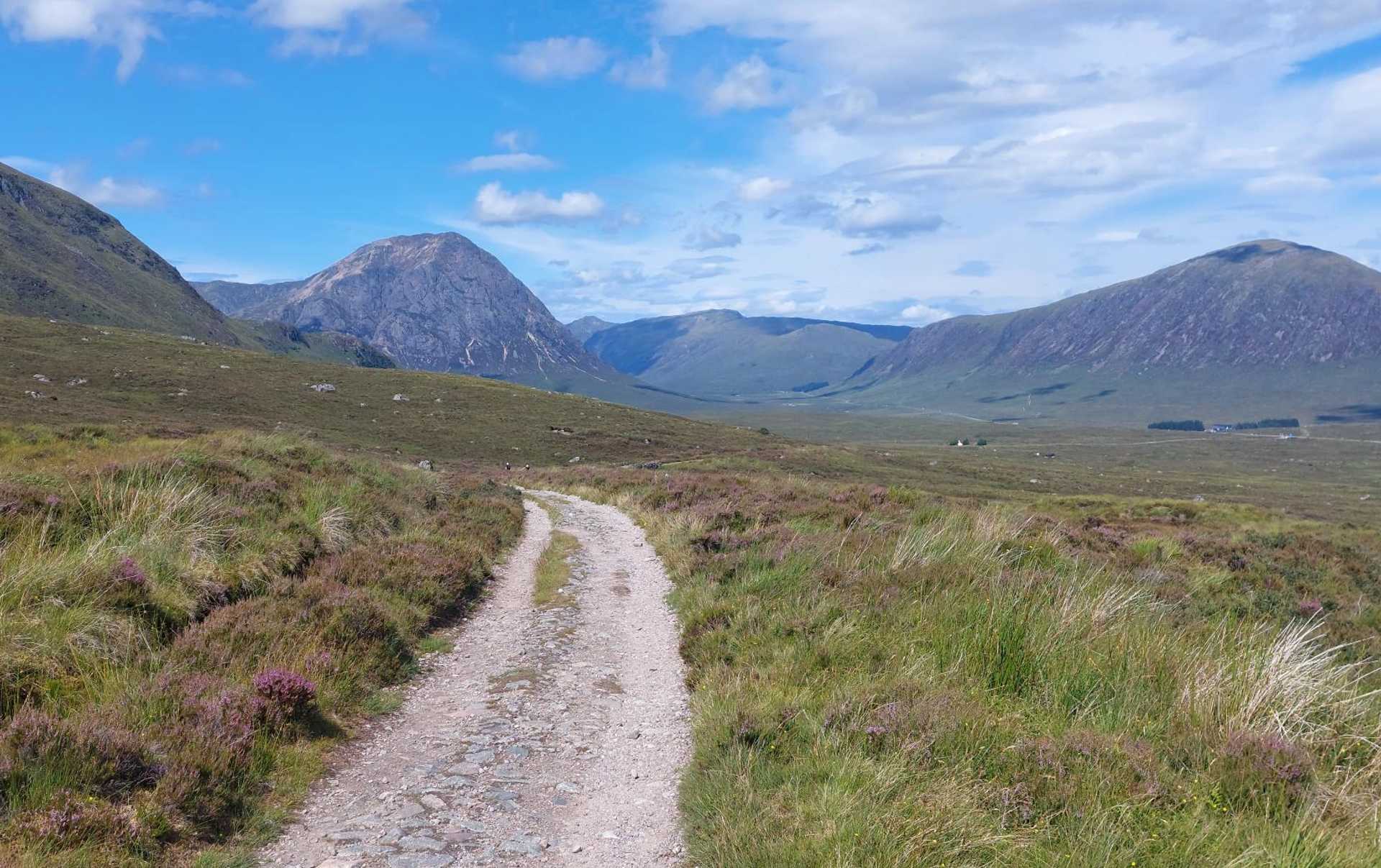 Broad stony track crossing open moorland on the West Highland Way, with Highland mountains ahead.