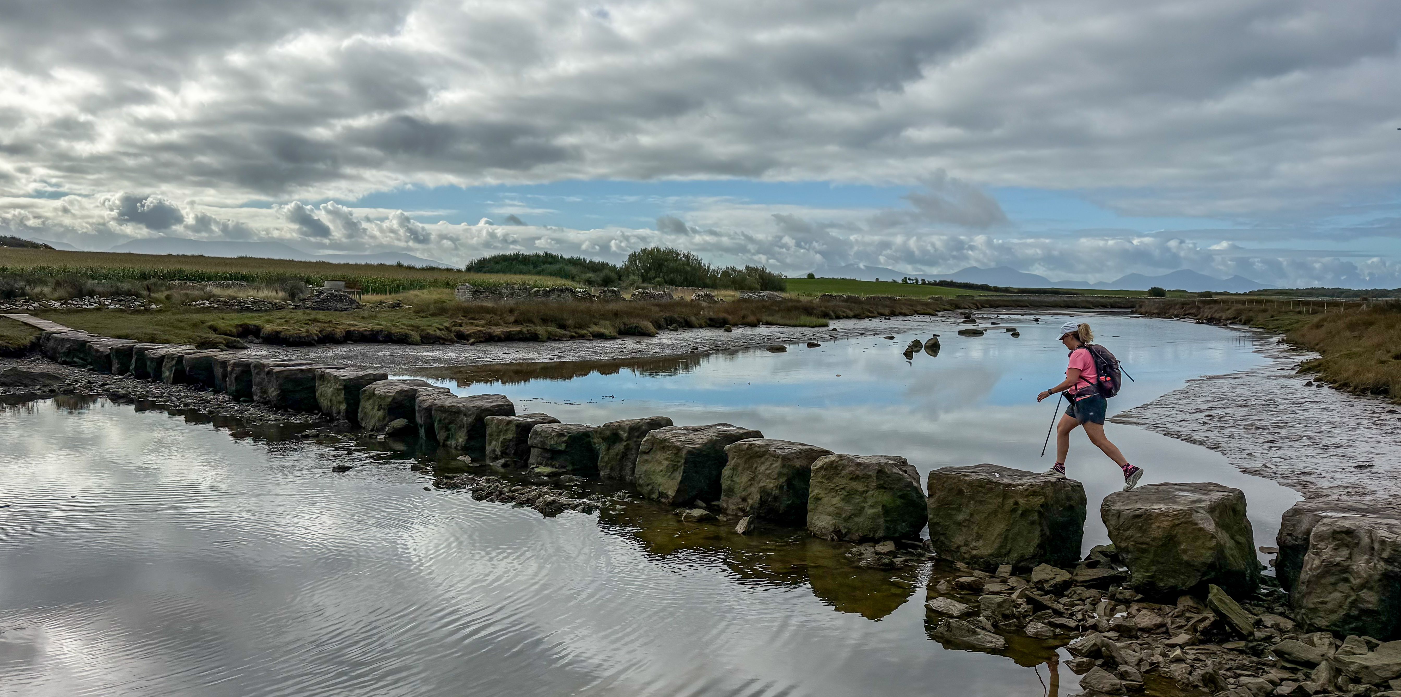 Walker crossing the Rhuddgaer Stepping Stones over the Afon Braint on the Anglesey Coast Path.
