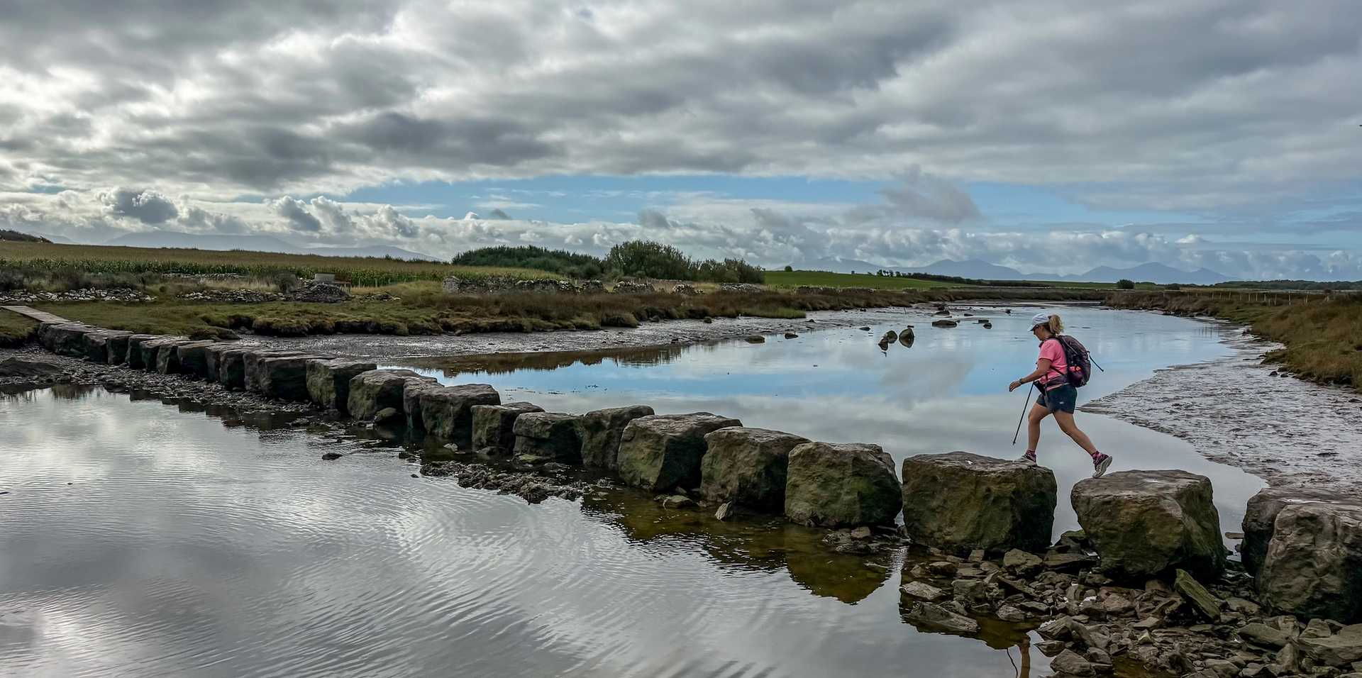Walker crossing the Rhuddgaer Stepping Stones over the Afon Braint on the Anglesey Coast Path.