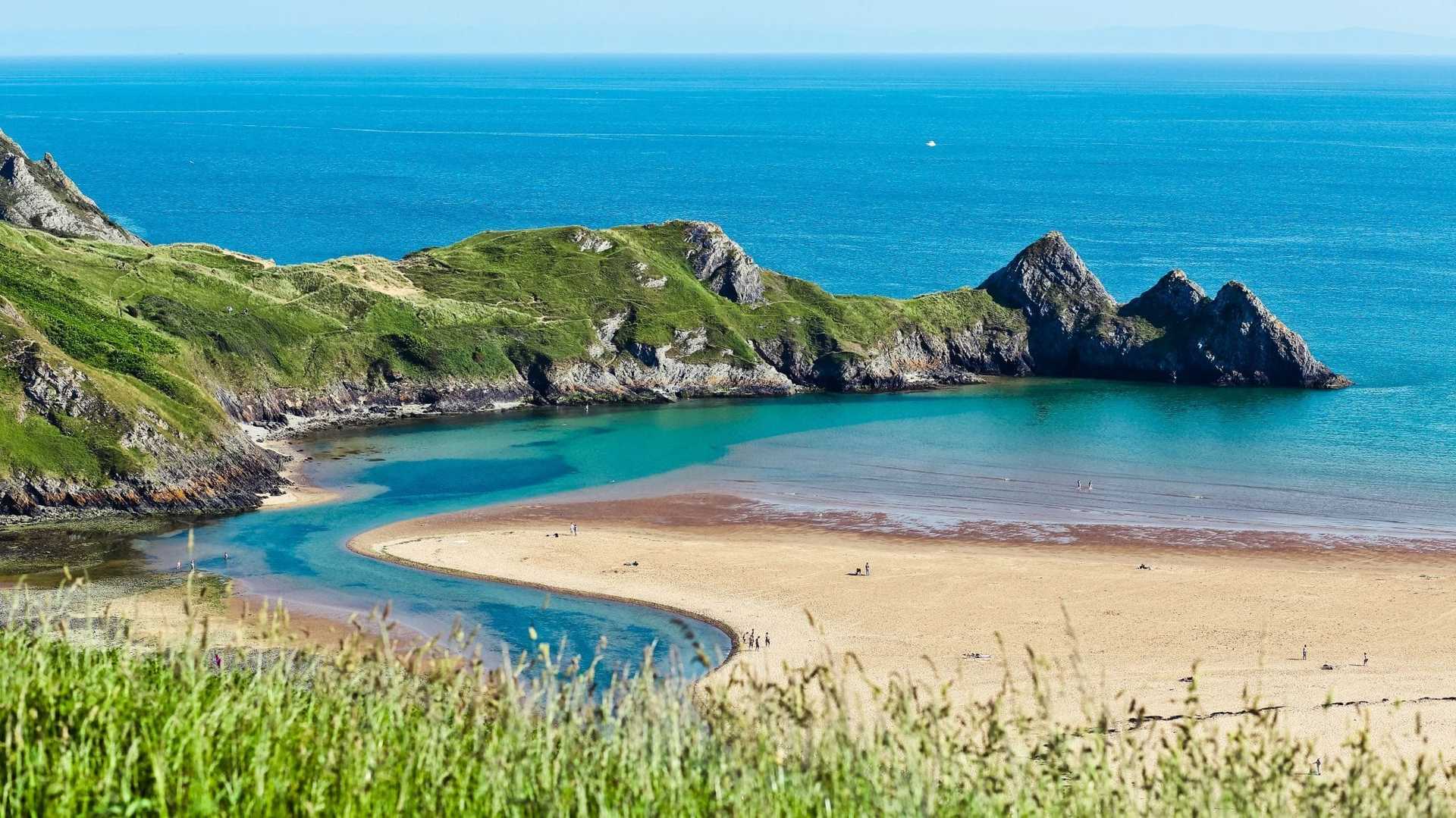 Three Cliffs Bay on the Gower Coast Path in Wales, with sandy beach, limestone cliffs and blue sea.