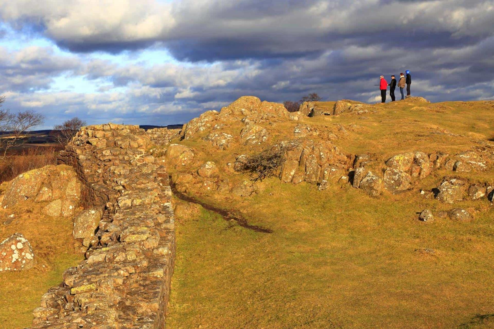 Walkers standing on the Whin Sill ridge beside Hadrian’s Wall in Northumberland