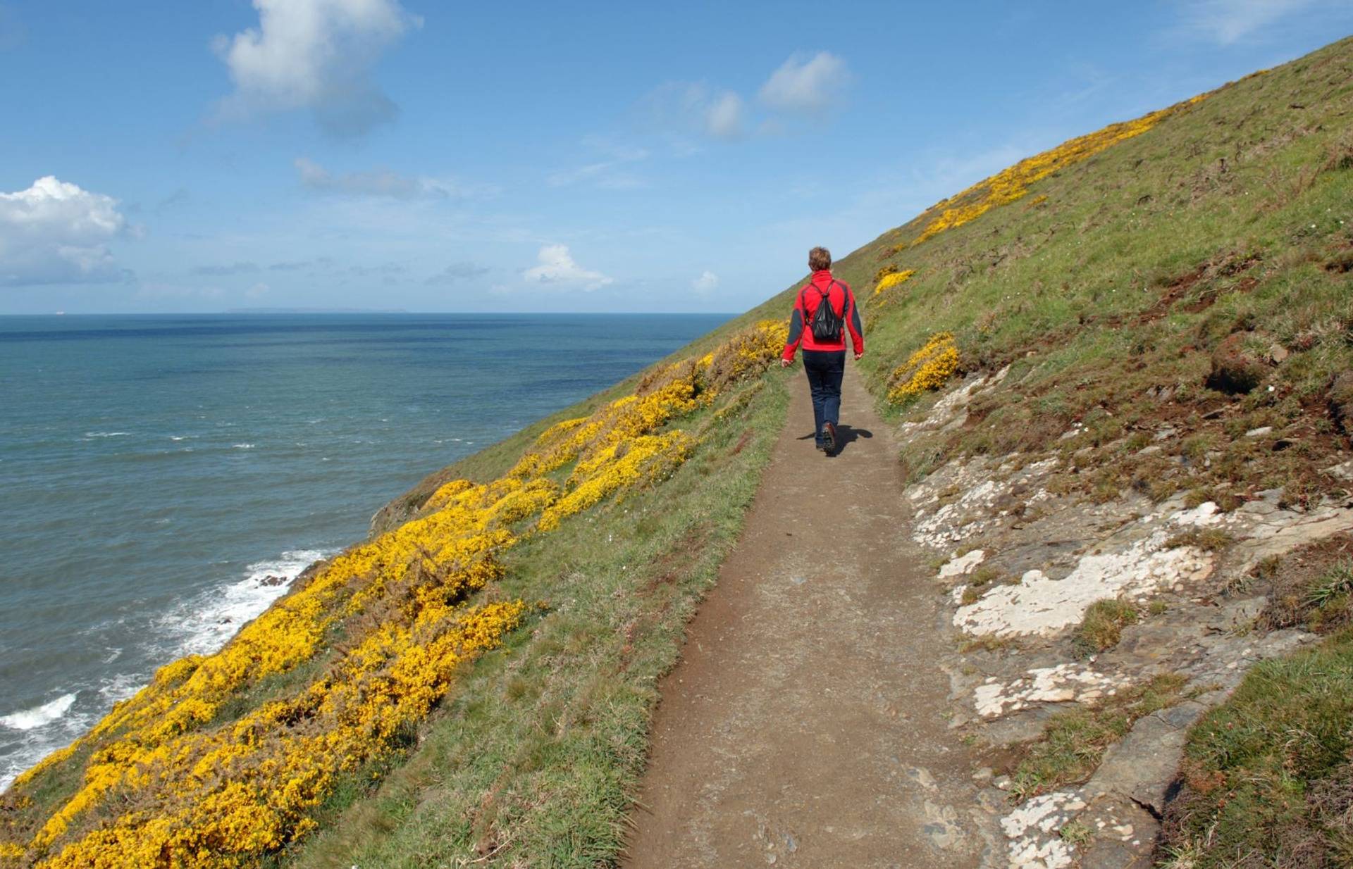 Walker following a coastal path with the sea and hillside ahead