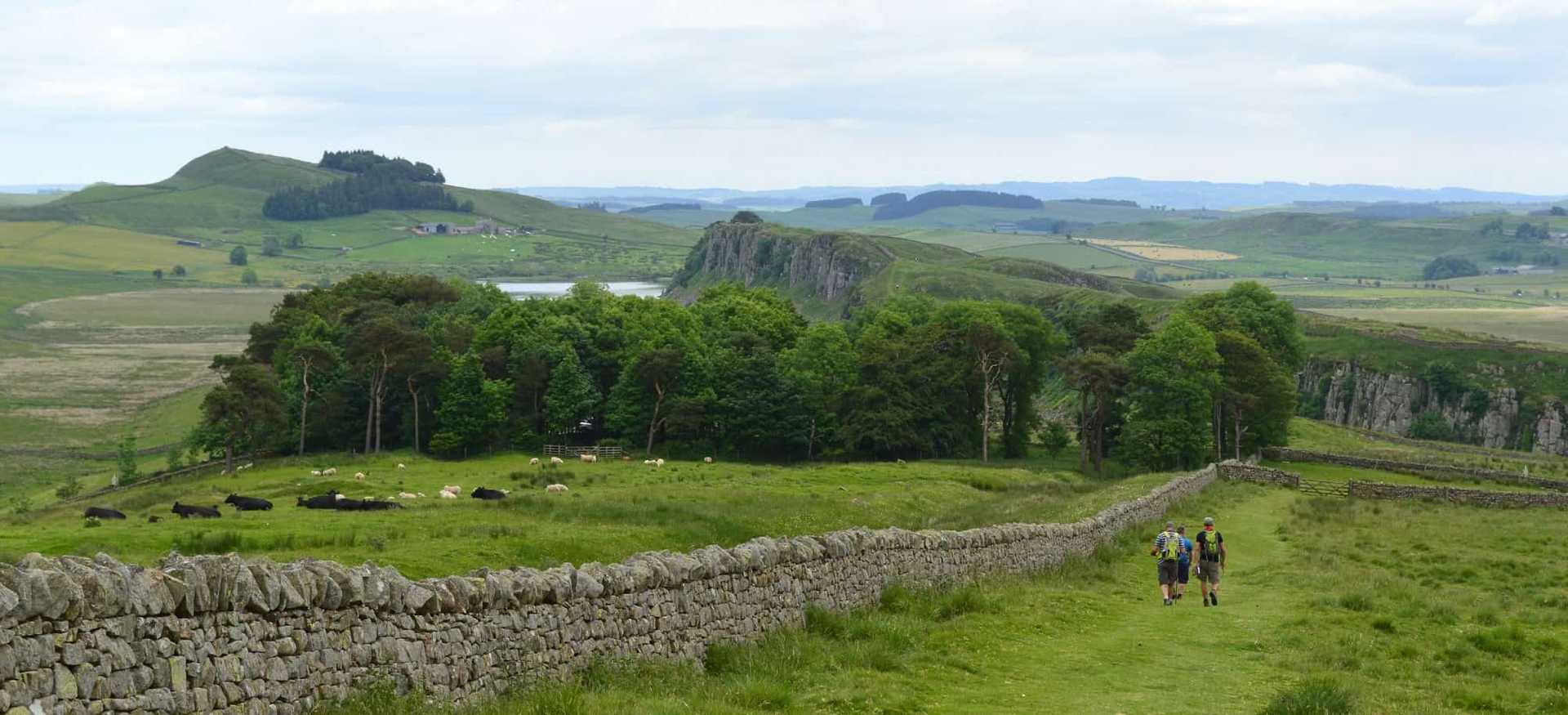 Walkers following Hadrian’s Wall across Northumberland farmland towards the Whin Sill ridge
