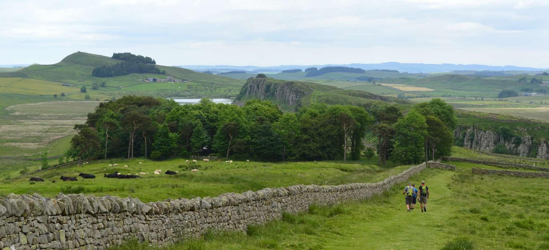 Walkers following Hadrian’s Wall across Northumberland farmland towards the Whin Sill ridge
